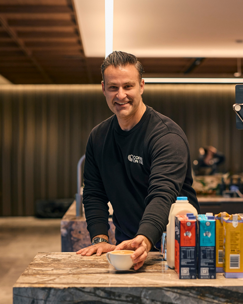 Barista handing a beautifully made coffee to a smiling office worker in a workplace cafe